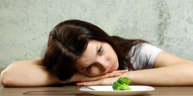 girl with head on table looking at broccoli