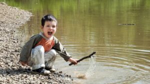 boy playing with stick in stream