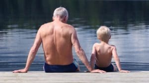 man and boy sitting on dock in twin trunks